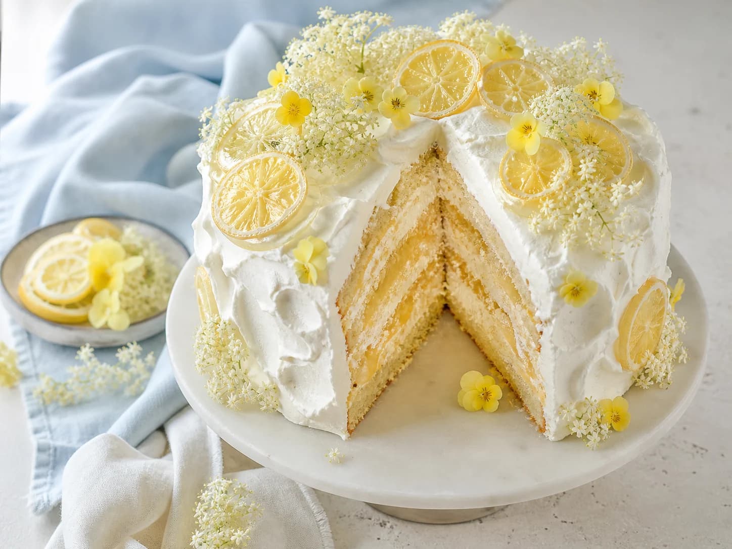 Eine elfenbeinfarbene Zitronen-Holunderblüten-Torte mit kandierten Zitronenscheiben